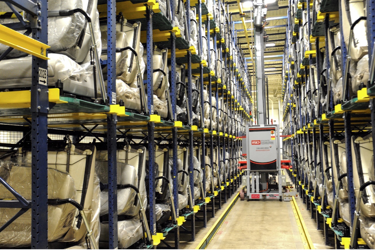 An organized warehouse features tall shelving units with wrapped goods and a central aisle occupied by an automated storage and retrieval solution.